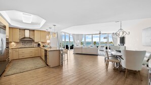 A modern kitchen with wooden cabinets, a central island, and a dining area with a white table and chairs. - Luxury Resort Spectacular Views of Cascading Pools and Bay; New Lazy River! Boat Slip! (Orange Beach)