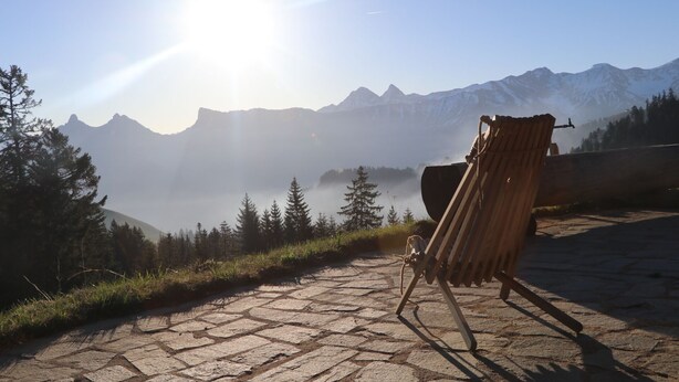 Una sedia di legno su un’area pavimentata in pietra, con vista sulle montagne sullo sfondo.