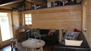 Un accogliente interno di una baita con pavimento in legno, uno sgabello rotondo in legno, un divano in pelle e una finestra con vista.