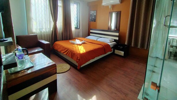 A hotel room with a bed, a desk, a chair, a water bottle, and a mirror.