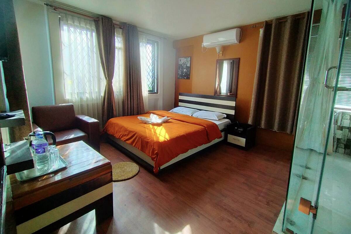 A hotel room with a bed, a desk, a chair, a water bottle, and a mirror.