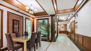 A spacious dining area with a glass-top table and multiple chairs, a brick accent wall, and a view of a green outdoor area. - Piyapruk Resort (Nakhon Ratchasima)