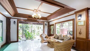 A spacious lobby with a high ceiling, wooden beams, and a chandelier. There are wicker furniture pieces and a large window providing a view of greenery outside. - Piyapruk Resort (Nakhon Ratchasima)