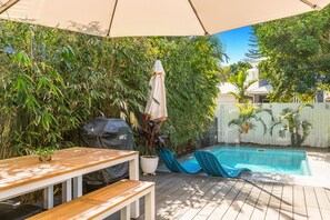 A backyard with a wooden deck, a barbecue grill, a pool with a slide, and a covered seating area.