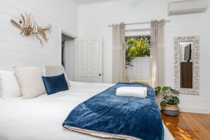 A bedroom with a large bed, white walls, a decorative fish wall art, a mirror, and a potted plant.