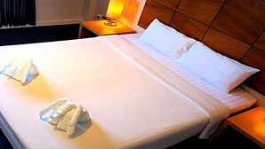 A neatly made bed with white linens, a bedside lamp, and a wooden headboard. - The Room Chaweng (Koh Samui)