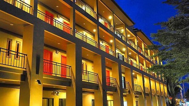 A multi-story hotel with balconies, a central staircase, and a tree in the foreground. - The Room Chaweng (Koh Samui)
