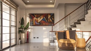 A modern interior with a staircase, a large abstract painting, and a wicker chair. - Modern 6BR House ⭐️City & Ocean Views from Jacuzzi (Cebu City)