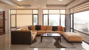 A modern living room with a sectional sofa, a coffee table, and large windows with blinds. - Modern 6BR House ⭐️City & Ocean Views from Jacuzzi (Cebu City)