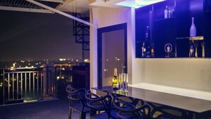 A rooftop bar with a glass railing, a table with chairs, and a shelf with bottles. - Modern 6BR House ⭐️City & Ocean Views from Jacuzzi (Cebu City)