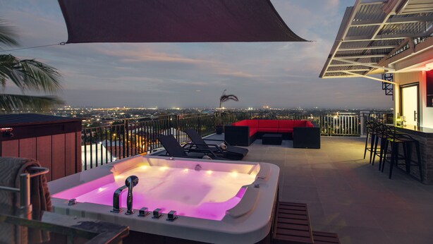 A rooftop terrace with a hot tub, seating area, and a view of the city at dusk. - Modern 6BR House ⭐️City & Ocean Views from Jacuzzi (Cebu City)