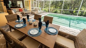 Ein Essbereich mit Tisch für vier Personen, mit Blick auf einen Swimmingpool, ausgestattet mit Korbmöbeln und modernem Interieur.