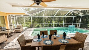 Ein überdachter Essbereich im Freien mit Pool, Korbmöbeln und Deckenventilator.