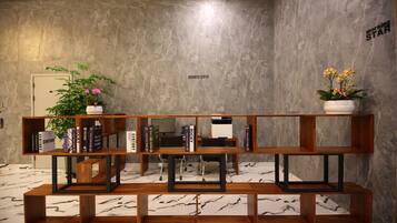 A modern interior with a marble floor, a wooden bookshelf with books and plants, and a sign reading "BUSINESS CENTER".