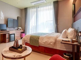 Habitación de hotel con cama, escritorio con televisor, cafetera y una mesita con bandeja.