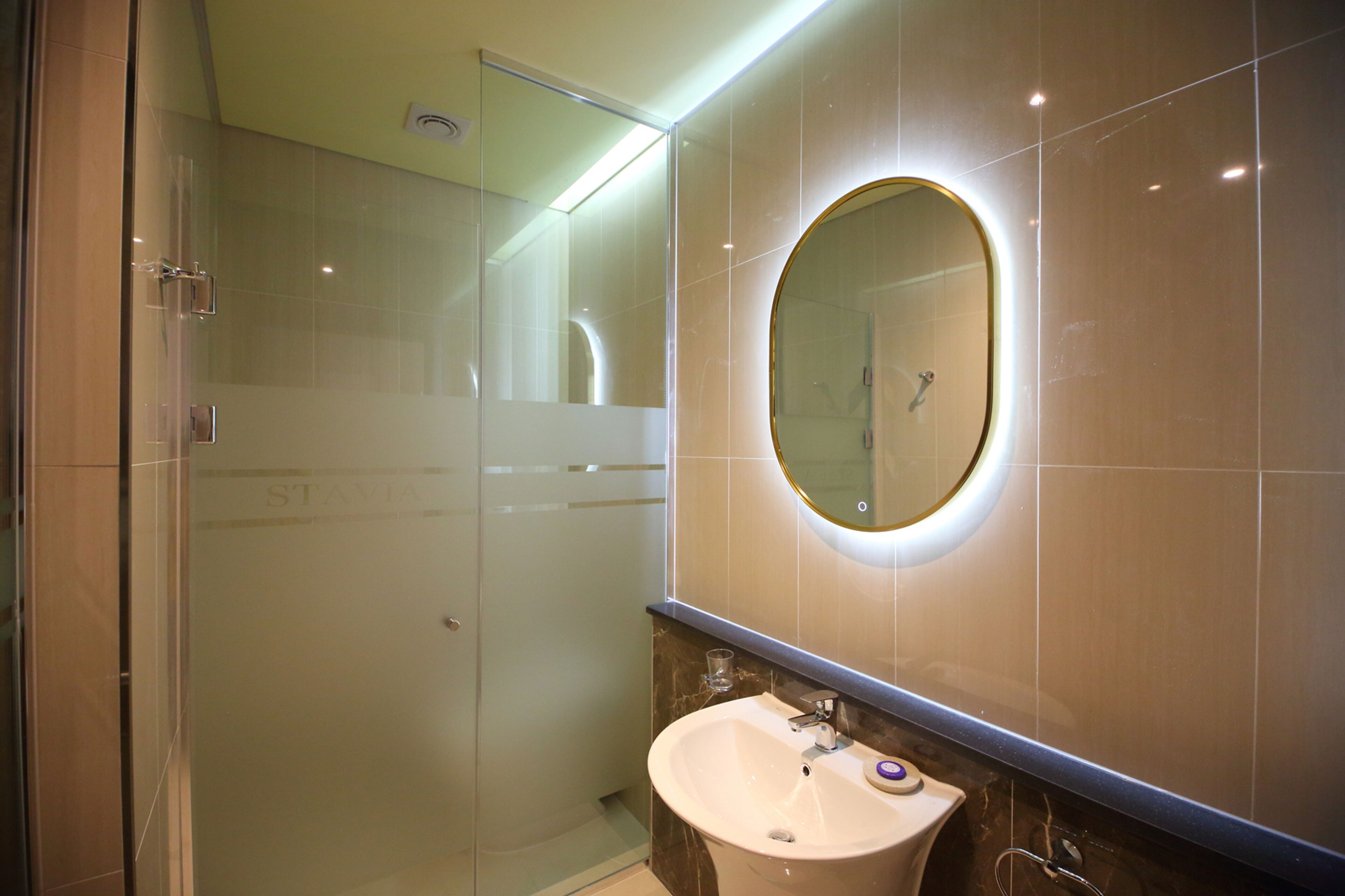 Une salle de bain moderne dotée d’une douche à parois de verre, d’un miroir rond avec un cadre doré et d’un lavabo surmonté d’un plan de travail en marbre.