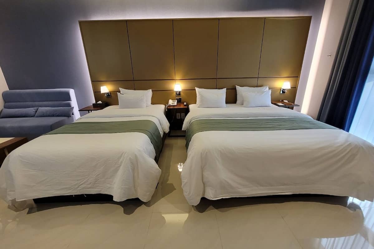 A hotel room with two beds, a blue chair, bedside tables with lamps, and a large headboard.