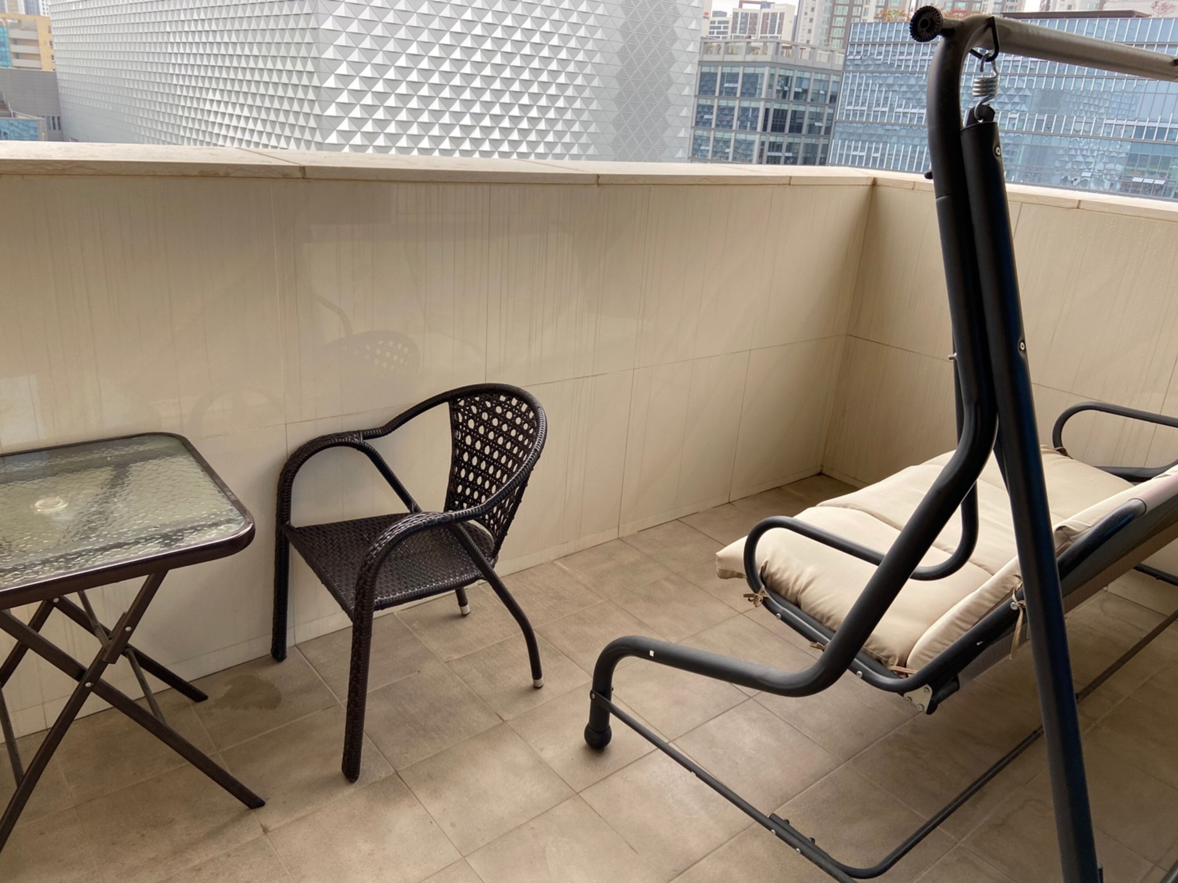 Un balcon avec une table en verre, une chaise en osier et un canapé pliable.
