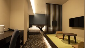 A hotel room with a bed, a desk, a chair, a table, and a TV.