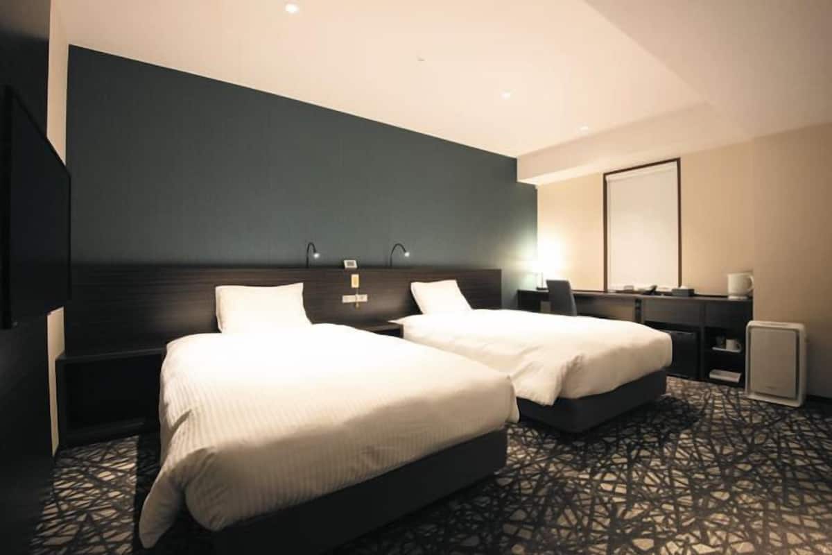 A hotel room with two beds, a dark headboard, a large mirror, and a patterned carpet.