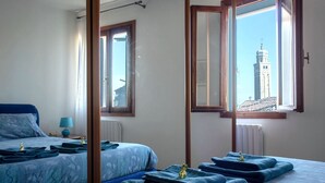 A bedroom with a bed, a nightstand, a lamp, and a view of a tower through a window. - Moira's House (Venezia)