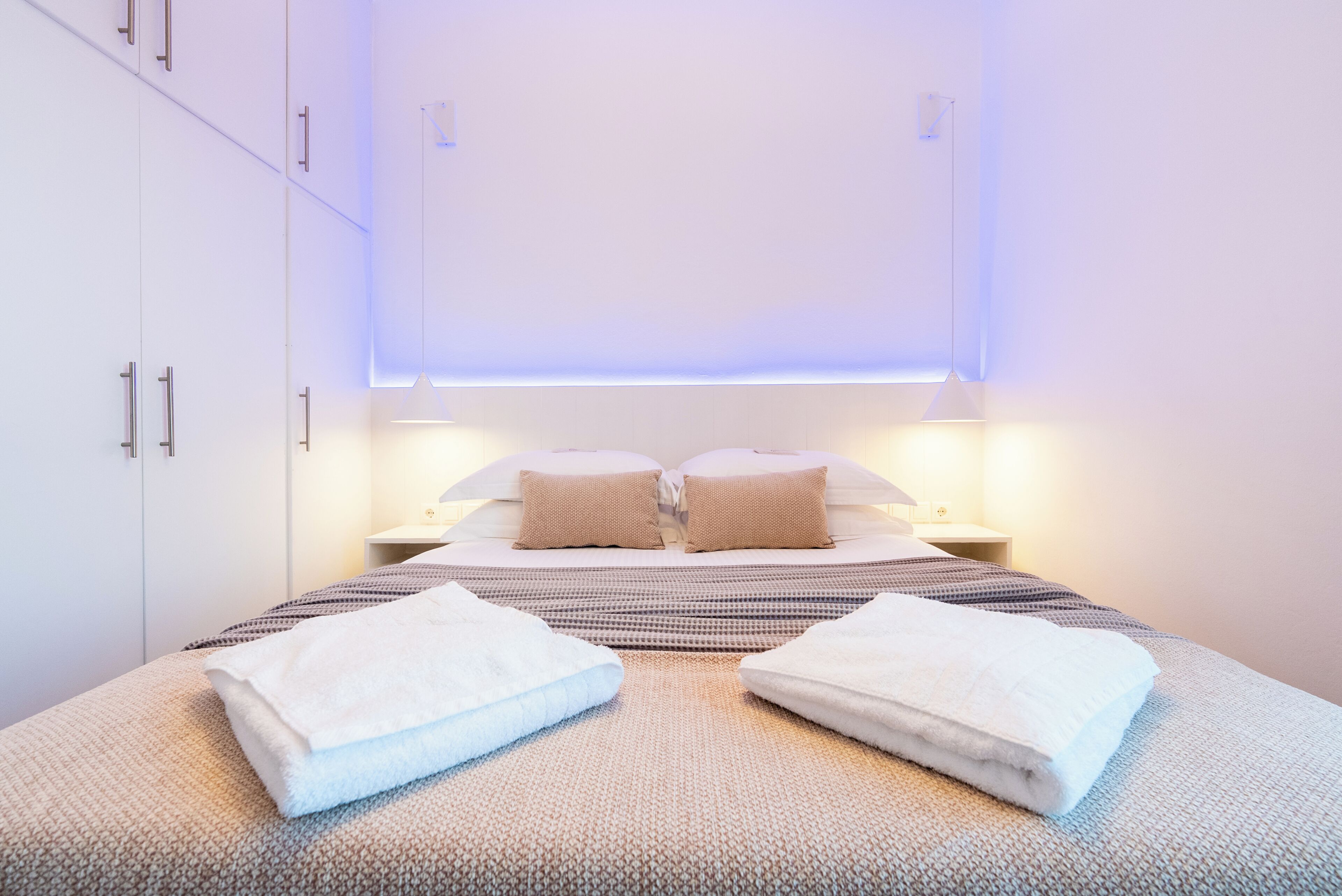 A modern hotel room with a large bed, two bedside tables, and a wardrobe.
