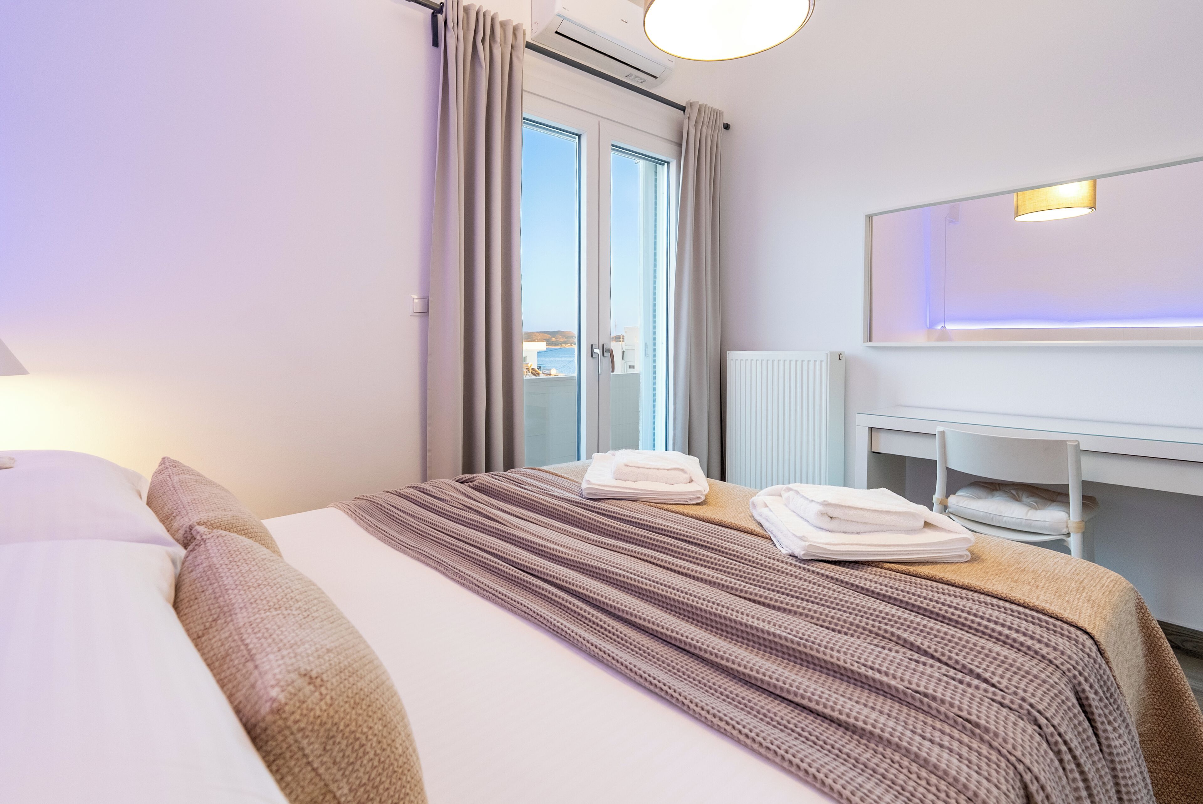 Ein Hotelzimmer mit Bett, Schreibtisch, Stuhl und Blick durch ein Fenster.