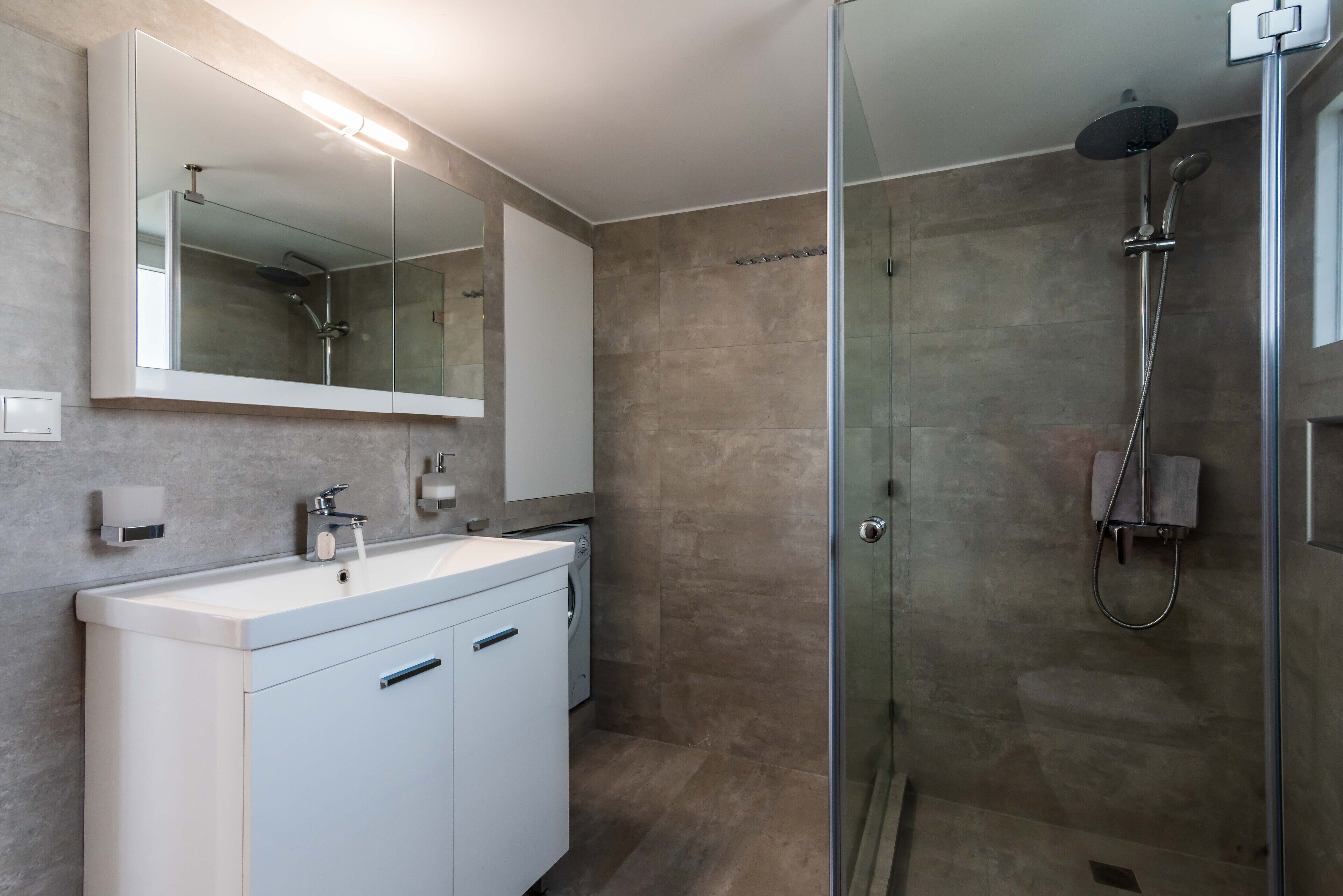 A modern bathroom with a glass-enclosed shower, a large mirror, and a white vanity with a sink.