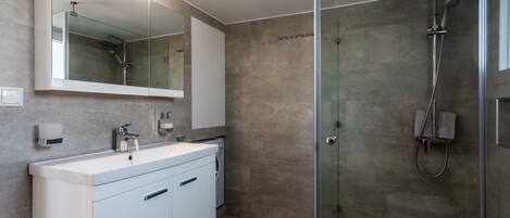 A modern bathroom with a glass-enclosed shower, a large mirror, and a white vanity with a sink.