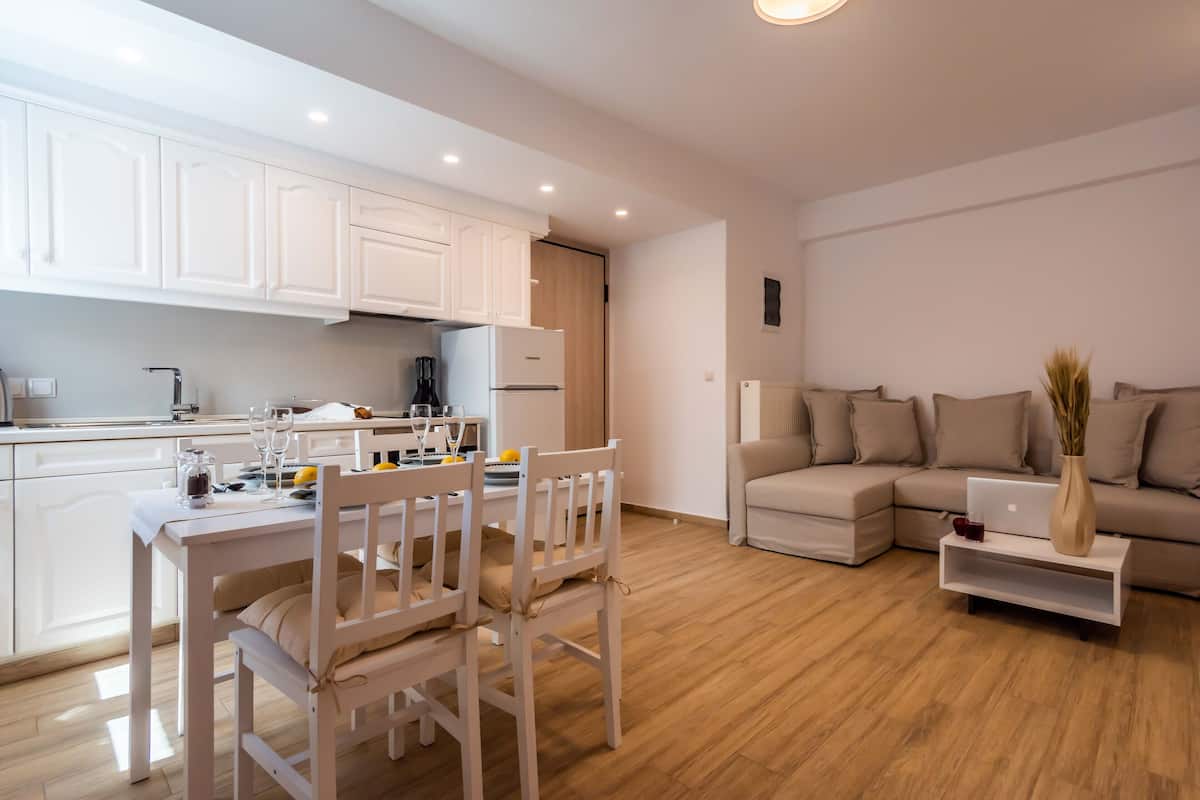 A modern kitchen with white cabinets, a dining table set with chairs, and a living area with a sofa and a laptop on a side table.