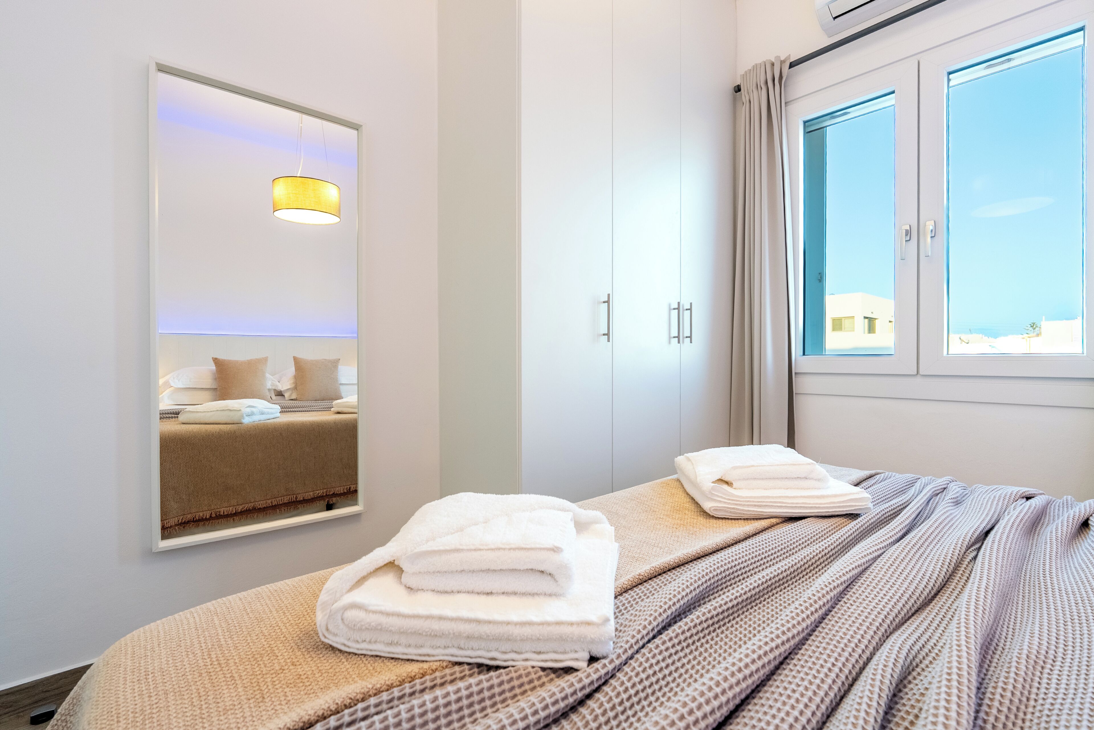 A hotel room with a bed, a mirror, a window, and a ceiling light.