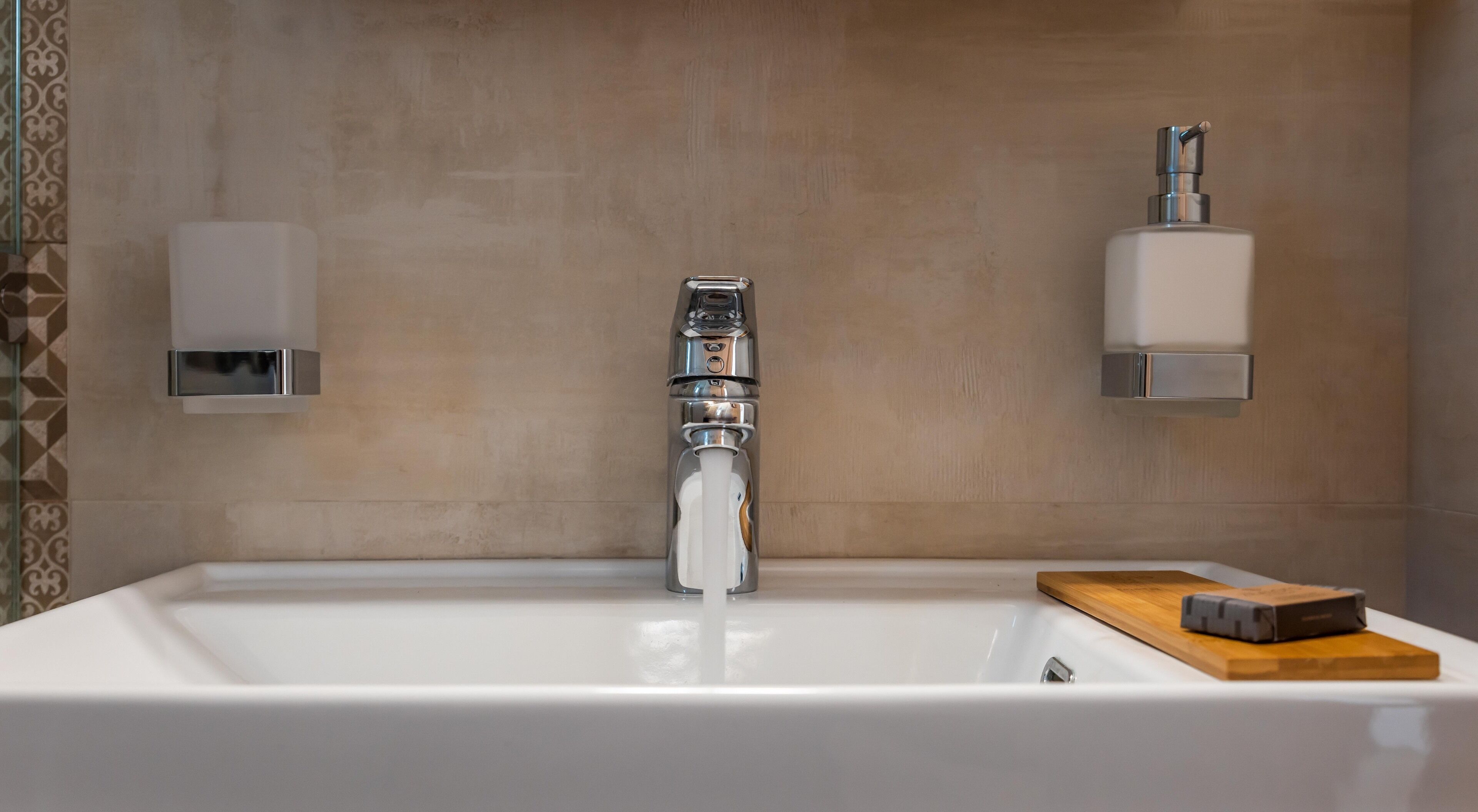 Une salle de bain avec un lavabo blanc, un robinet moderne et deux distributeurs de savon fixés au mur.