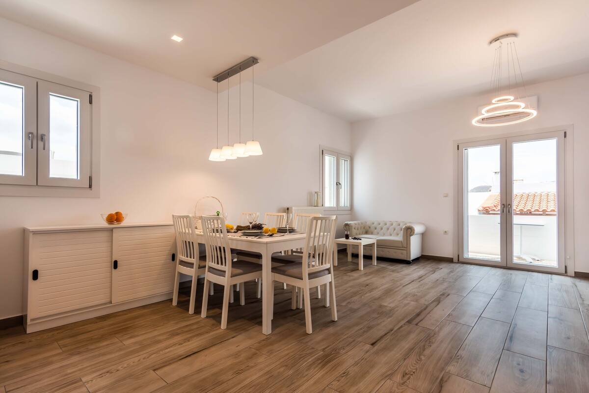 A spacious room with a dining table and chairs, a sofa, and a large sliding glass door to the outside.