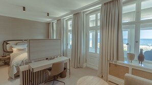 Et hotelværelse med en seng, et skrivebord, en stol, et rundt bord og store vinduer med gardiner.