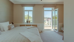 A bedroom with a large bed, two windows, a radiator, and a view of the outside.