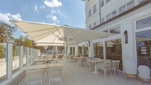 An outdoor cafe area with tables and chairs, large umbrellas, and a view of the street.