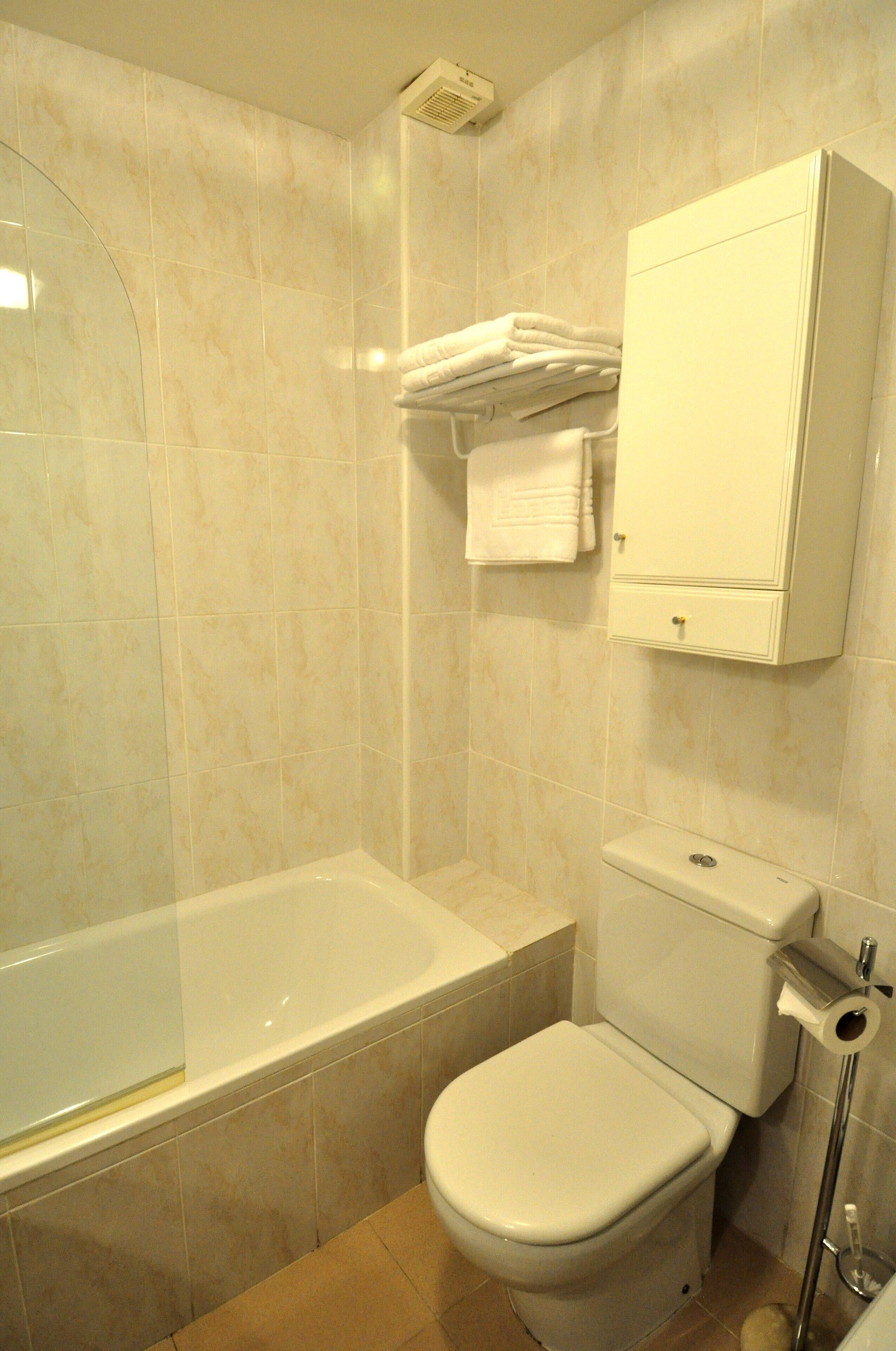 Un baño con bañera, inodoro y toallero con toallas dobladas.