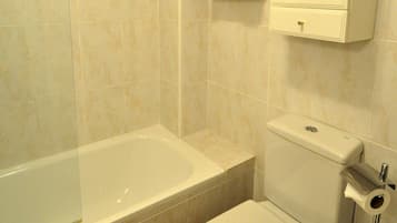 Un baño con bañera, inodoro y toallero con toallas dobladas.