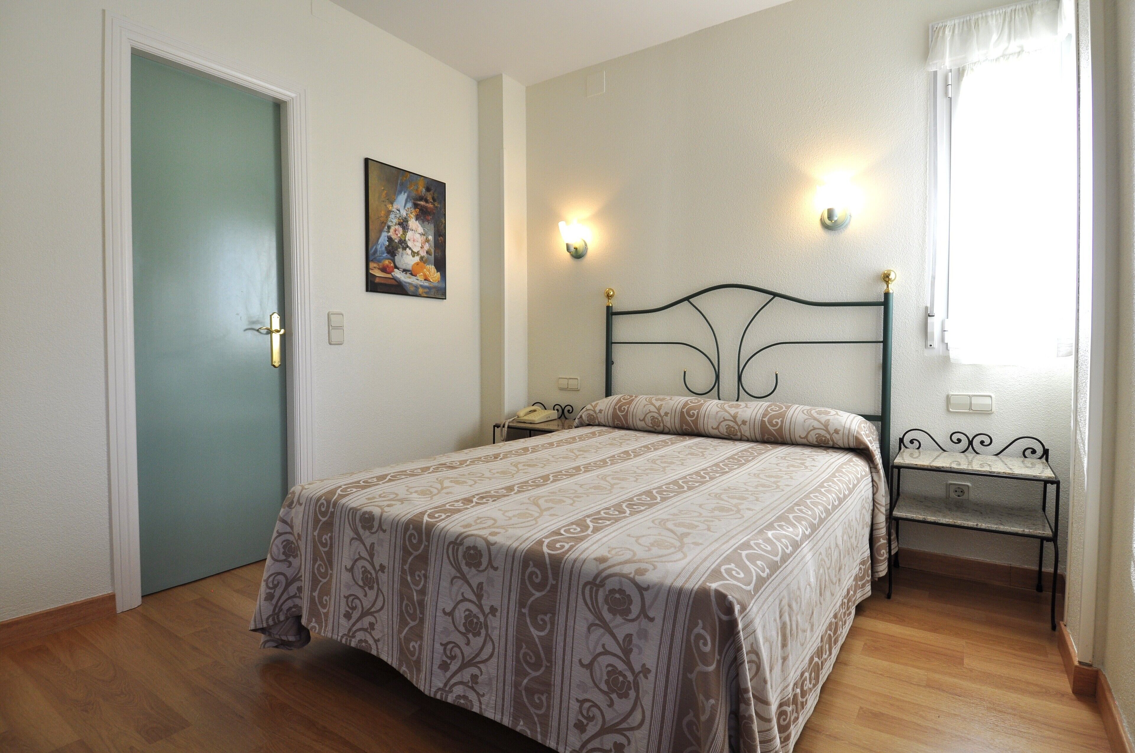 Un dormitorio con cama, mesitas de noche, un cuadro y una puerta.