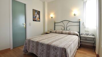 Un dormitorio con cama, mesitas de noche, un cuadro y una puerta.
