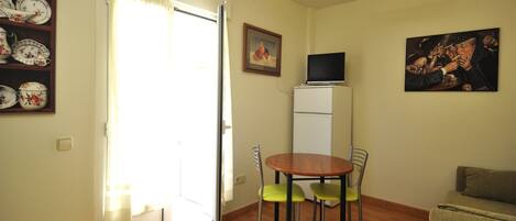 Un comedor con una mesa y sillas, un televisor sobre un mueble, un cuadro en la pared y una puerta que da a otra habitación.