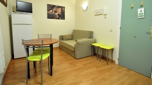 Un espace de vie compact comprenant une table à manger, des chaises, un canapé et un petit téléviseur posé sur un meuble.