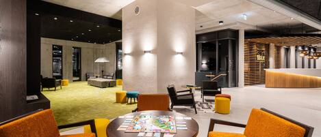 A modern lobby with a round table, orange chairs, and a board game.