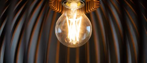 A light bulb with a clear glass enclosure, suspended from a ceiling with a ribbed, dark background.