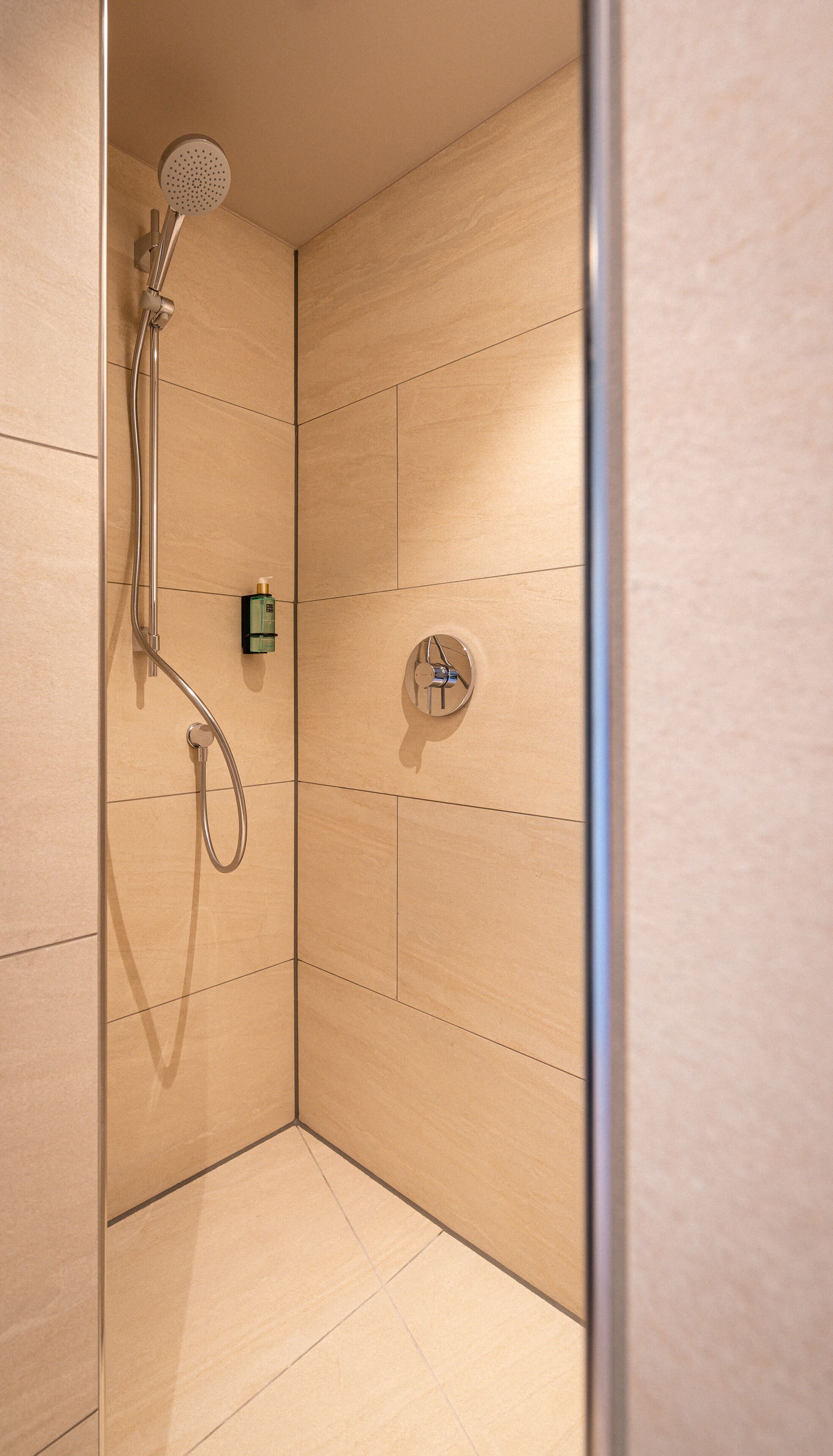 A shower with a handheld showerhead and a wall-mounted control panel.