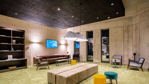 Un área de estar moderna con un sofá, reposapiés y sillones, una estantería y un televisor.