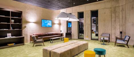 A modern lounge area with a sofa, ottoman, and chairs, a bookshelf, and a television.
