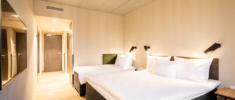 Ein Hotelzimmer mit zwei Betten, einem großen Spiegel und Holzboden.