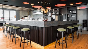 Un área de bar moderna con una isla central, varios taburetes e iluminación colgante.