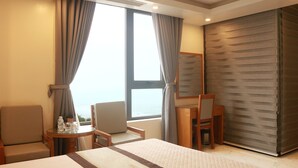Hotelkamer met een bed, een stoel, een klein tafeltje met een fles en glazen, en uitzicht op de zee door grote ramen.